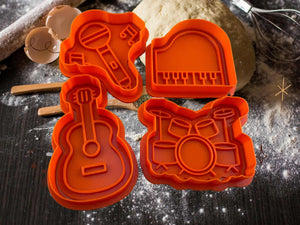 Musik Keks-Ausstecher Set mit Gitarre, Mikrofon, Klavier und Schlagzeug in Orange auf einem Backuntergrund.