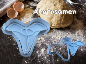Keks-Ausstecher in Form von Ahornsamen auf einer bemehlten Oberfläche, ideal fürs Herbstbacken.