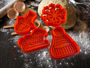 Weihnachtliche Keks-Ausstecher in Form von Schneemann, Schneeflocke, Schlitten und Mütze auf einem Teiguntergrund.