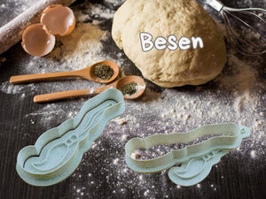 Halloween Besen Keks-Ausstecher auf bemehlter Arbeitsfläche mit Teig und Gewürzen, perfekt für gruselige Backabenteuer.