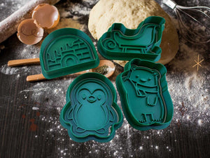Winter cookie cutters in shapes of penguin, polar bear, sled, and igloo on a baking surface with dough.
