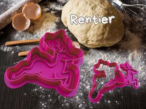 Weihnachtlicher Keks-Ausstecher in Rentier-Form auf einem bemehlten Tisch mit Teig und Kochutensilien.