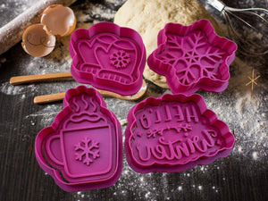 Purple winter-themed cookie cutters on a baking table, featuring designs of a glove, snowflake, mug, and 'Hello Winter' text.