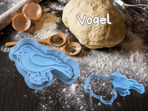 Herbstliche Keks-Ausstecher in Form eines Vogels neben Keksteig und Backutensilien auf einer Holzoberfläche.