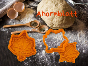 Herbst Keks-Ausstecher in Form von Ahornblättern auf einem Küchentisch mit Teig und Zutaten.