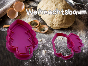 Set of pink Christmas tree cookie cutters on a floured table with dough and baking tools.