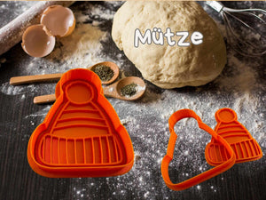 Wintermütze Keksausstecher auf Teig mit Küchenutensilien, ideal für festliche Weihnachtskekse.