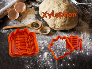 Musik Keks-Ausstecher Set für Xylophon, gezeigt auf bemehltem Backtisch mit Teig, Eierschalen und Gewürzen.