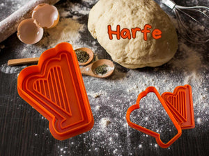 Orange harp cookie cutter on kitchen counter with dough, ready for baking musical-themed cookies.