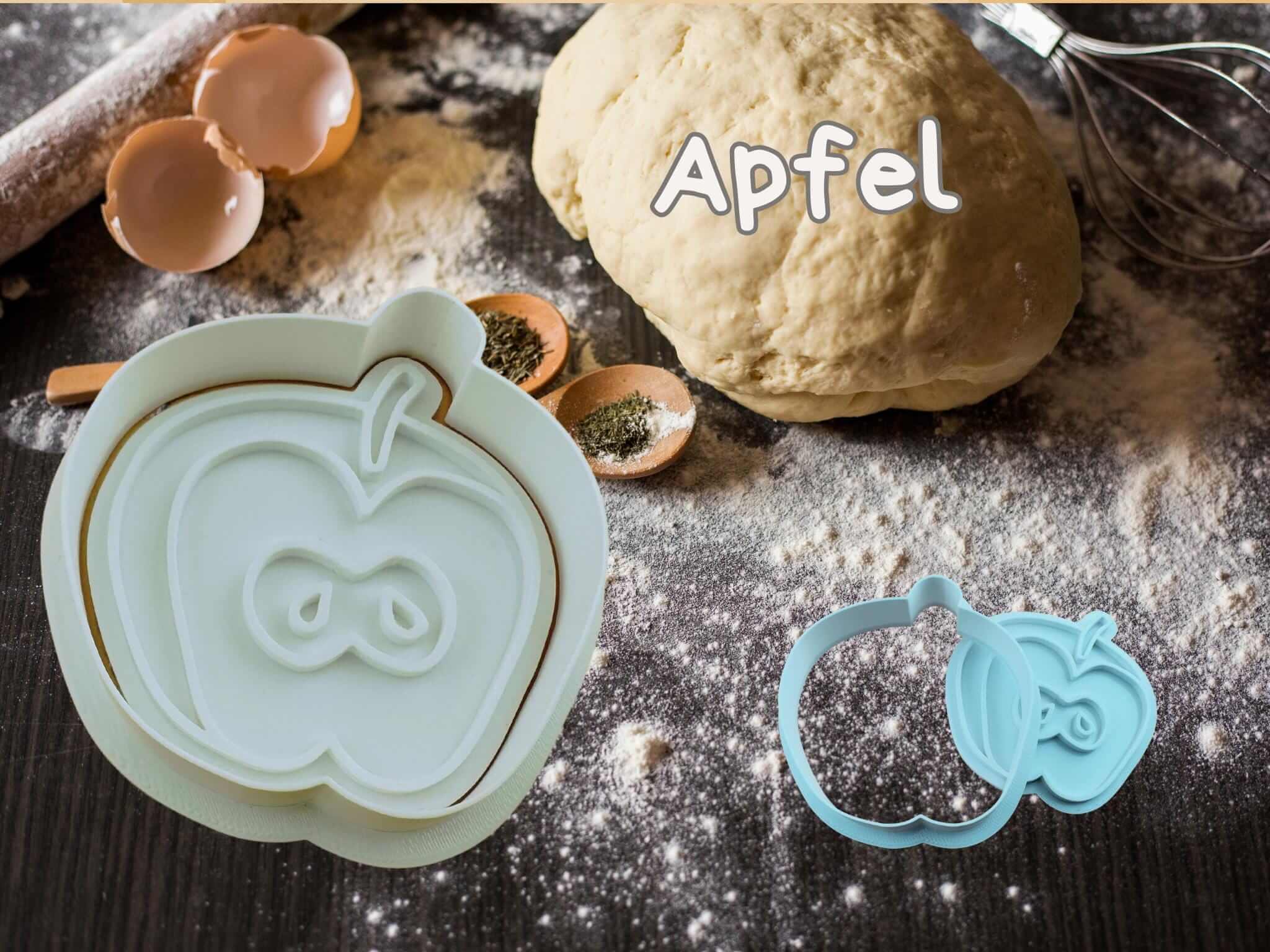 Apple-shaped cookie cutter with dough and baking ingredients, perfect for creating autumn-themed treats.
