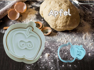 Apple-shaped cookie cutter with dough and baking ingredients, perfect for creating autumn-themed treats.