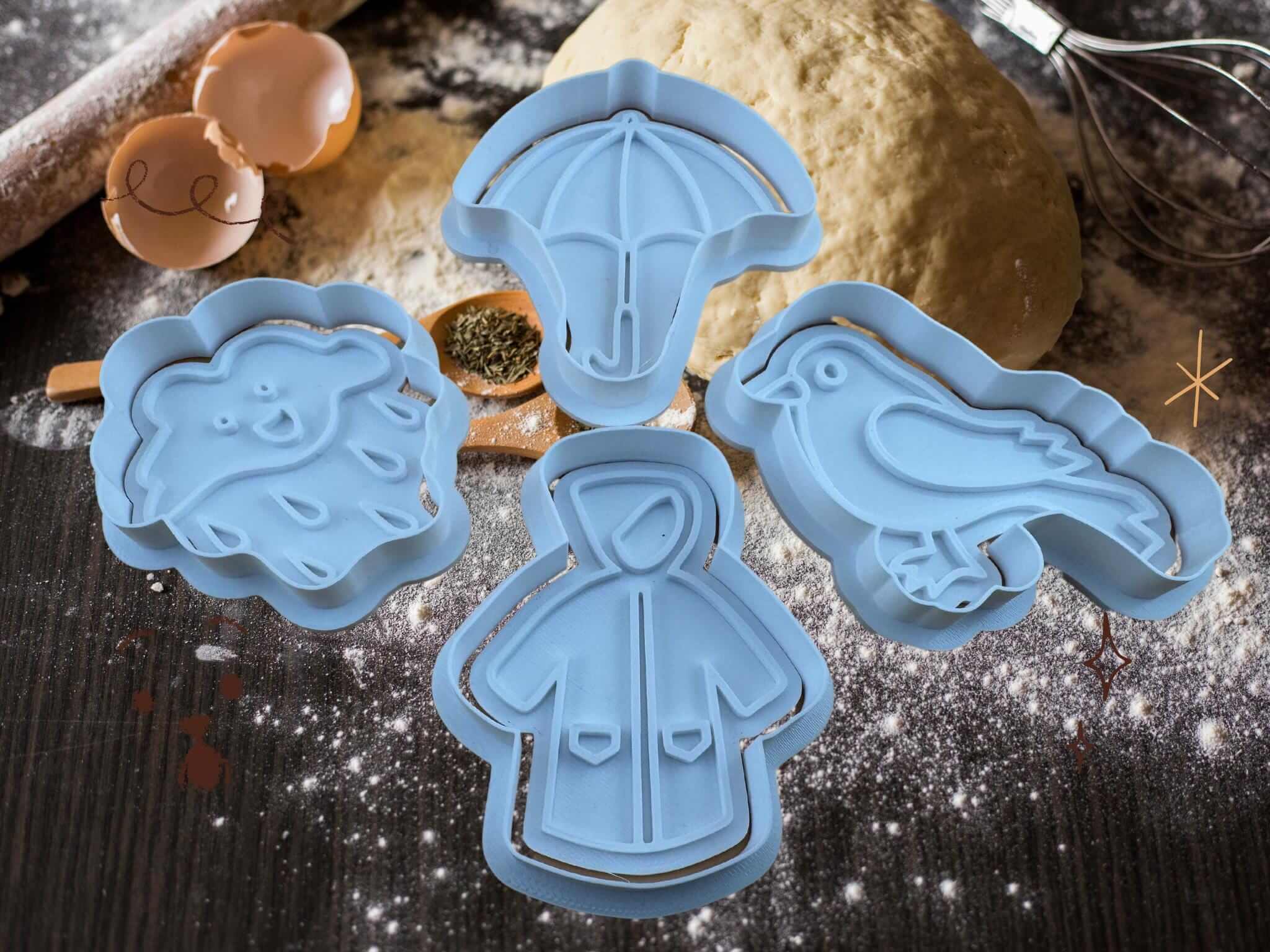 Herbstliche Keks-Ausstecher in Wolken-, Regenschirm-, Vogel- und Regenmantel-Designs auf einer Backoberfläche.