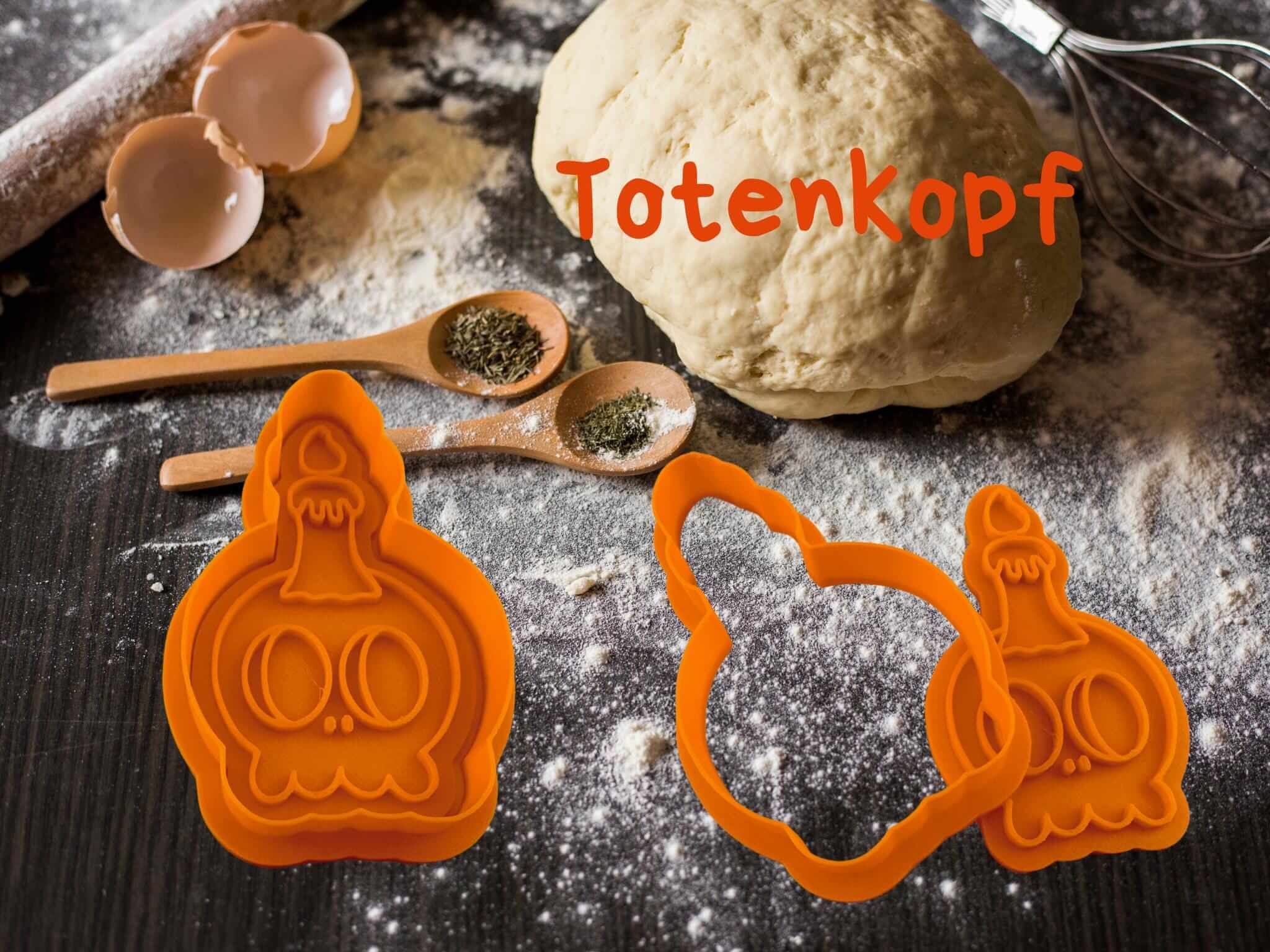 Orange Totenkopf-Ausstecher für Halloween-Kekse neben Teig und Backzubehör auf dunklem Untergrund